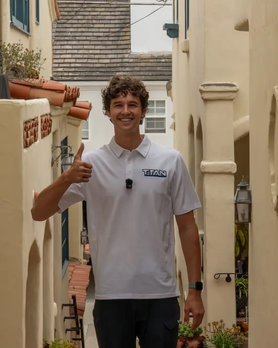 Titan crew member in a Titan shirt giving a thumbs up outside a stucco home